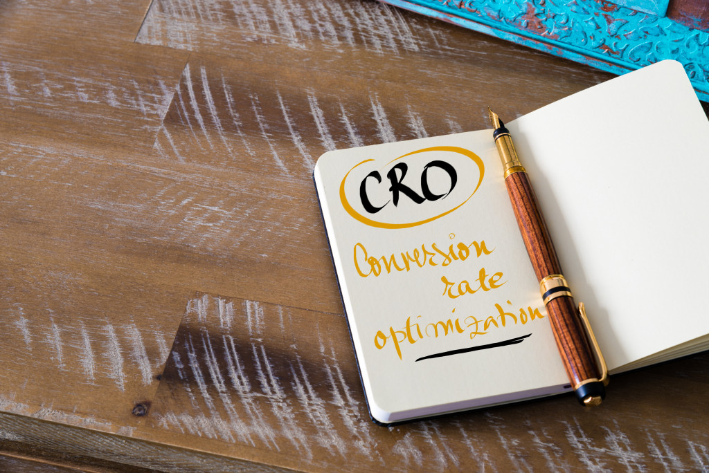 Retro effect and toned image of notebook next to a fountain pen. Business acronym CRO CONVERSION RATE OPTIMIZATION with handwritten text