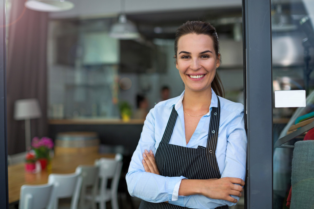 a woman wearing apron smiling in the door to a restaurant