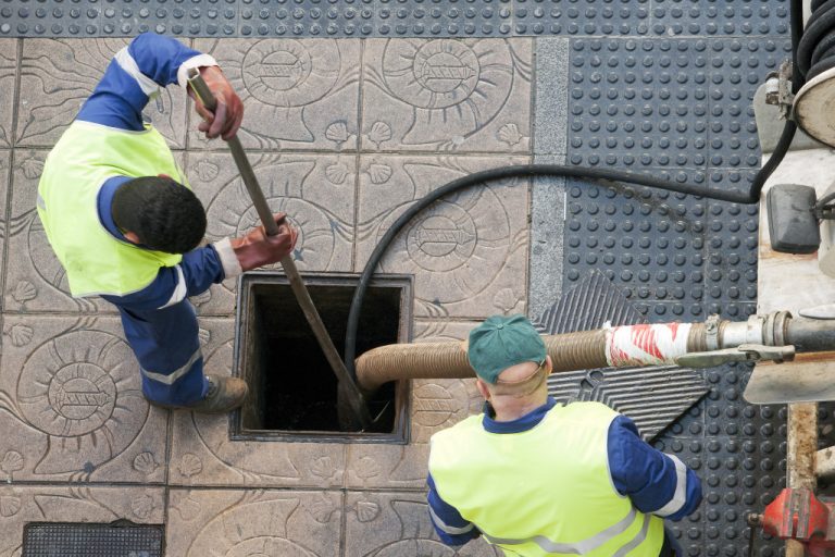 Utility workers moves the manhole cover to clean the sewer line for clogs